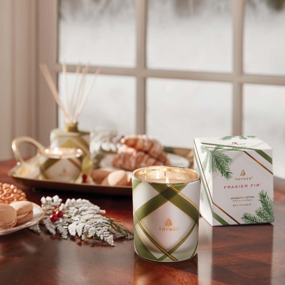 Thymes Frasier Fir Frosted Plaid Votive Candle is a Christmas Candle being lit on kitchen table image number 1